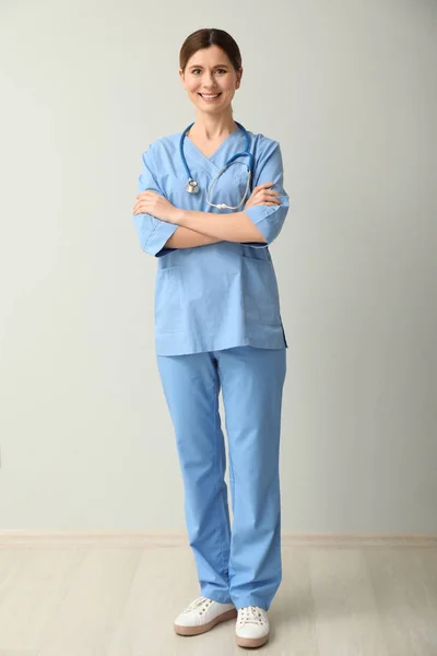 Beautiful female doctor near light wall — Stock Photo, Image