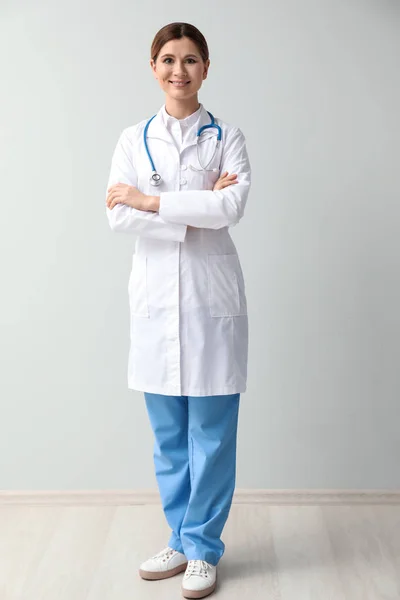 Beautiful female doctor near light wall — Stock Photo, Image