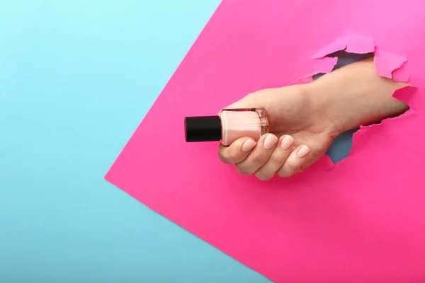 Female hand with nail polish visible through torn paper