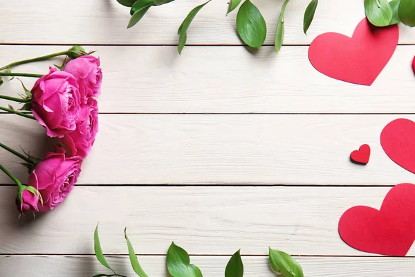 Hermosas rosas con corazones de papel sobre fondo blanco de madera — Foto de Stock