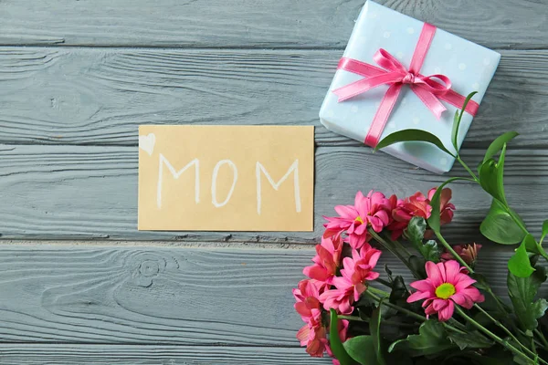 Tarjeta de felicitación con flores y regalo para el día de la madre en la mesa de madera —  Fotos de Stock