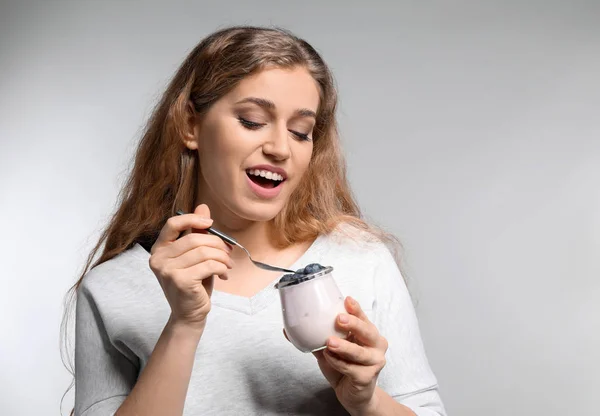 Junge Frau isst leckeren Joghurt auf hellem Hintergrund — Stockfoto