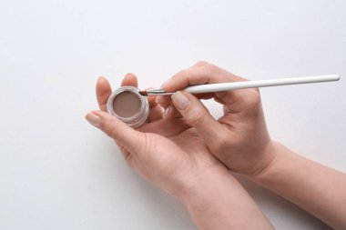 Işık arka planda kaş düzeltmesi için fırça ve boya ile kadın eller