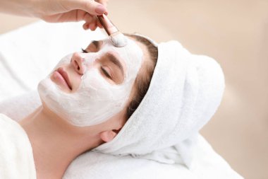 Kozmetik uzmanı güzellik salonundaki kadının yüzüne maske takıyor.