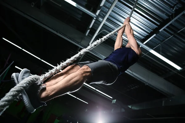 Young sporty man climbing up the rope in gym — Stock Photo, Image