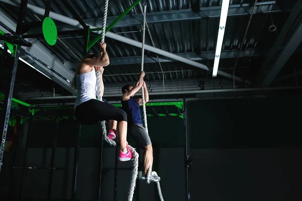 Jeune couple sportif grimpant la corde dans la salle de gym — Photo