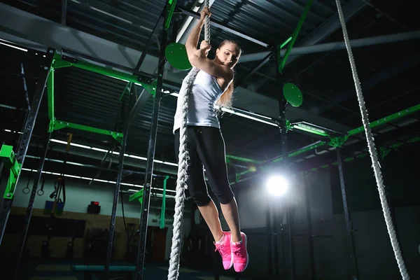 Молодая спортсменка карабкается по веревке в спортзале — стоковое фото