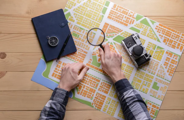 Male hands with city map, magnifier, compass and photo camera on wooden table — Stock Photo, Image