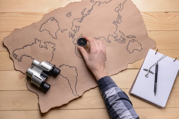 Male hand with world map, compass and binocular on wooden background