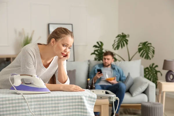 Triest huisvrouw Strijkservice kleren terwijl haar luie echtgenoot rusten op Bank — Stockfoto