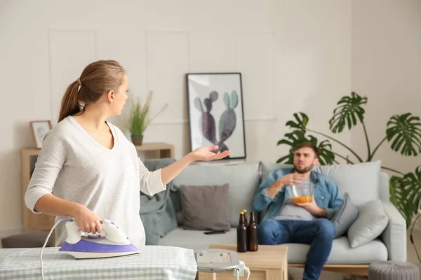 Housewife with iron scolding her lazy husband resting on couch — Stock Photo, Image