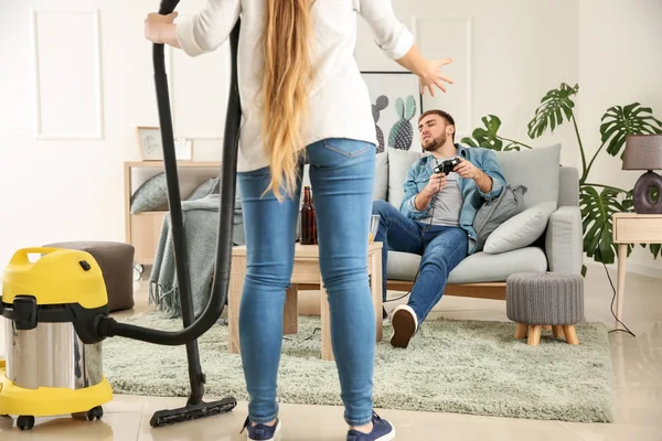Wife with vacuum cleaner scolding her lazy husband at home — Stock Photo, Image