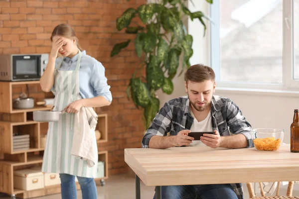 Lazy husband using mobile phone while his tired wife doing chores — Stock Photo, Image