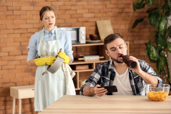 Luie man met behulp van mobiele telefoon, terwijl zijn vrouw doet klusjes — Stockfoto