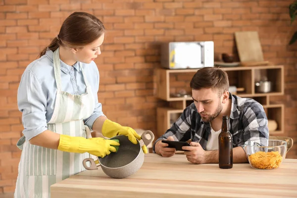 Luie man met behulp van mobiele telefoon, terwijl zijn vrouw doet klusjes — Stockfoto