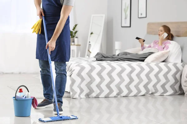 Househusband cleaning floor near lazy wife lying in bed — Stock Photo, Image