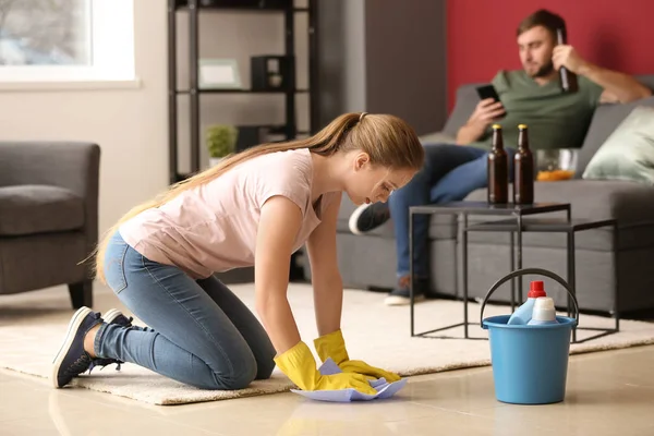 Wife cleaning floor while her lazy husband resting on couch at home — Stock Photo, Image