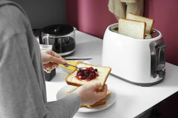Woman eating tasty toasted bread with jam in kitchen