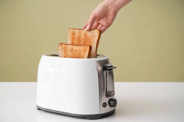 Woman taking bread slice from toaster on table — Stock Photo, Image