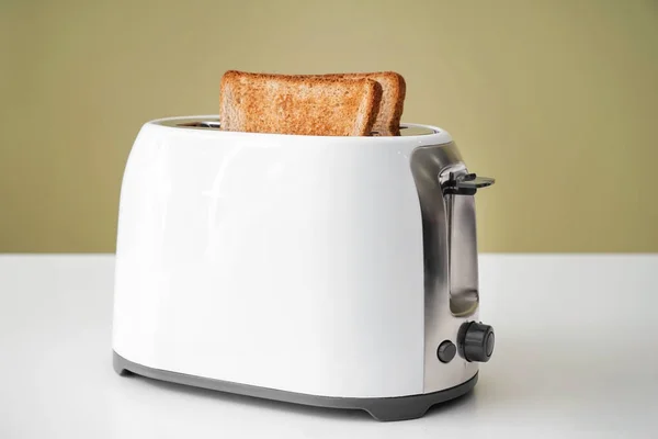 Toaster with bread slices on table against color background — Stock Photo, Image