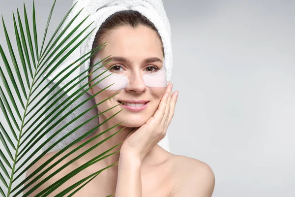 Mujer con parches bajo los ojos y hoja tropical sobre fondo claro —  Fotos de Stock