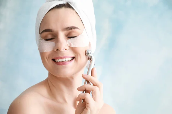 Mujer con parches bajo los ojos y herramienta de masaje facial sobre fondo claro —  Fotos de Stock