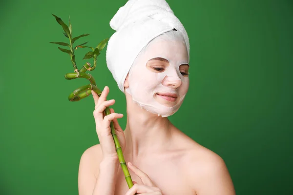 Woman with sheet facial mask and bamboo branch on color background — Stock Photo, Image