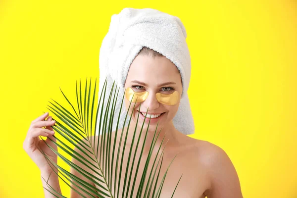 Young woman with under-eye patches and tropical leaf on color background — Stock Photo, Image