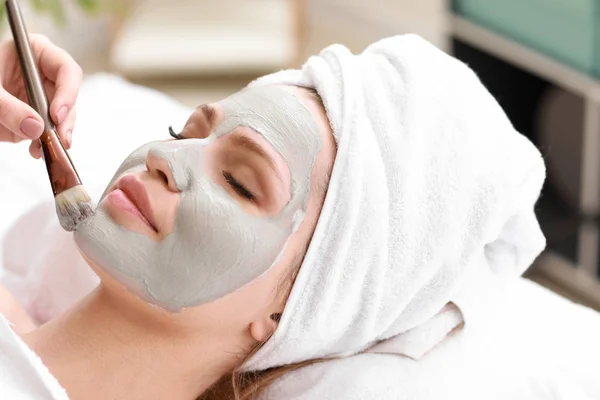 Cosmetólogo aplicación de máscara en la cara de la mujer joven en el salón de belleza — Foto de Stock