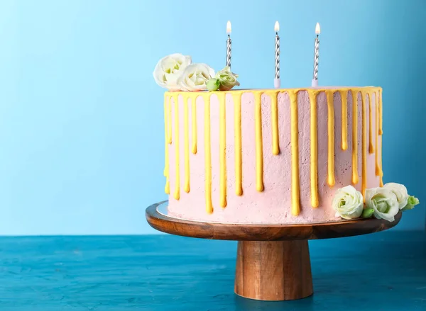 Leckeren Kuchen mit brennenden Kerzen auf Farbtisch — Stockfoto