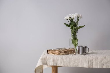 Hafif arka plana karşı masada eski kitap ve kupa ile taze çiçekler