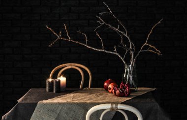 Ağaç dalları kavanoz ve koyu arka plan karşı masada mumlar ile nar