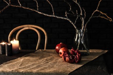 Ağaç dalları kavanoz ve koyu arka plan karşı masada mumlar ile nar