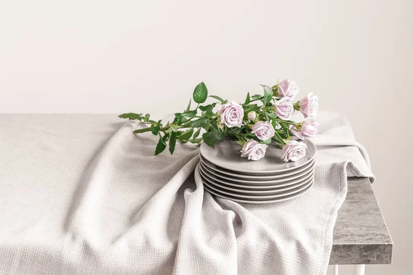 Стек чистих тарілок зі свіжими трояндами на столі на світлому фоні — стокове фото