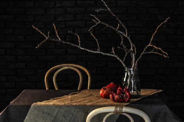 Pomegranates with tree branches in jar on table against dark background — Stock Photo, Image