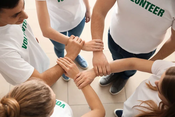 Team of young volunteers holding hands together indoors — Stock Photo, Image