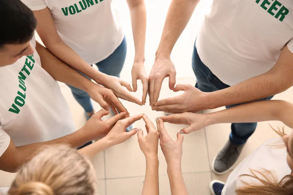 Zespół młodych wolontariuszy trzymając ręce razem pomieszczeniu — Zdjęcie stockowe