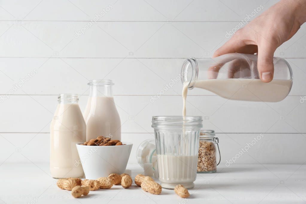Man pouring tasty vegan milk from bottle into glass on white table