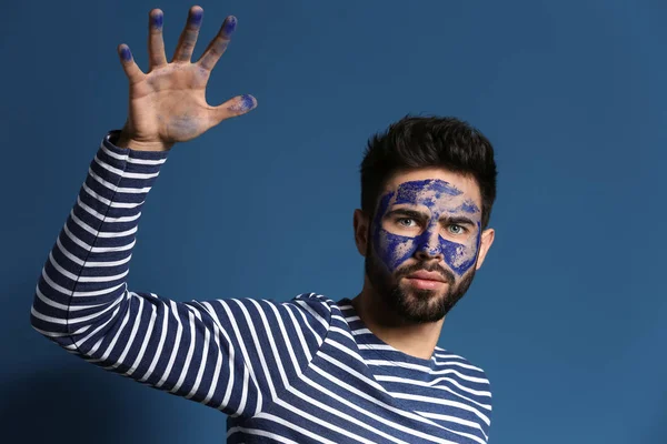 Portrait of handsome man with paint on his face and hand against color background — Stock Photo, Image