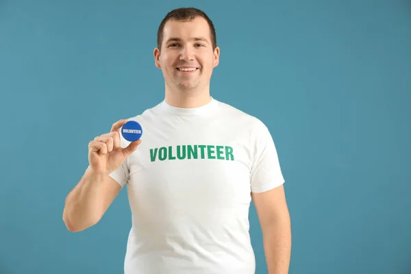 Young male volunteer with badge on color background — Stock Photo, Image