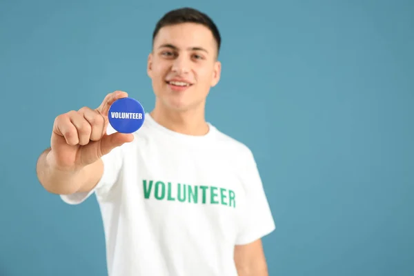 Young male volunteer with badge on color background — Stock Photo, Image