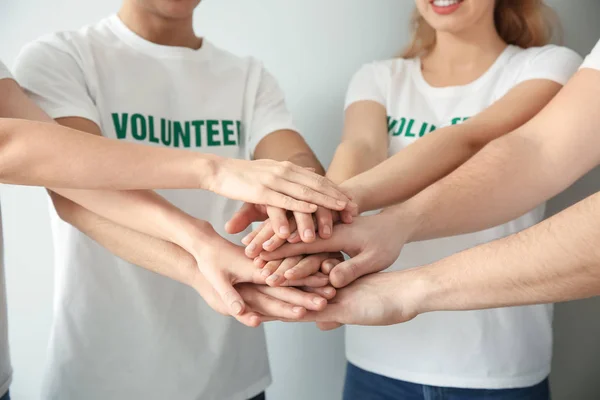 Team of young volunteers putting hands together on light background — Stock Photo, Image