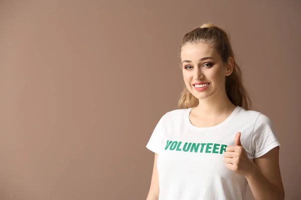 Unga kvinnliga frivilliga visar tummen upp på färgbakgrund — Stockfoto