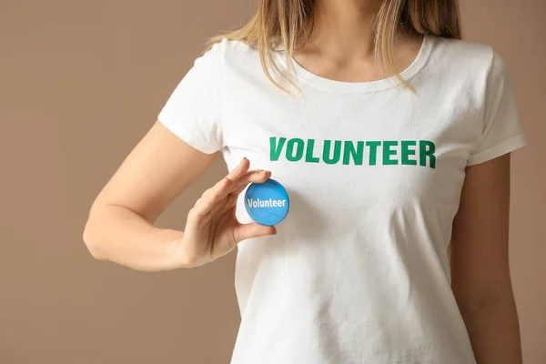 Young female volunteer with badge on color background