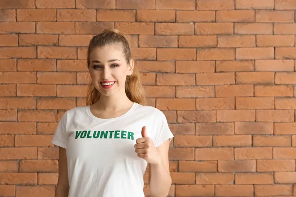 Young female volunteer showing thumb-up against brick wall — Stock Photo, Image