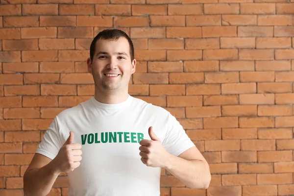 Young male volunteer showing thumb-up against brick wall — Stock Photo, Image