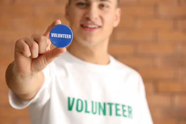 Young male volunteer with badge against brick wall — Stock Photo, Image