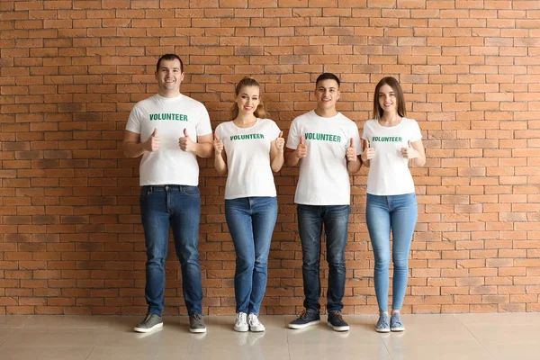Team av unga volontärer visar tummen upp mot tegelvägg — Stockfoto