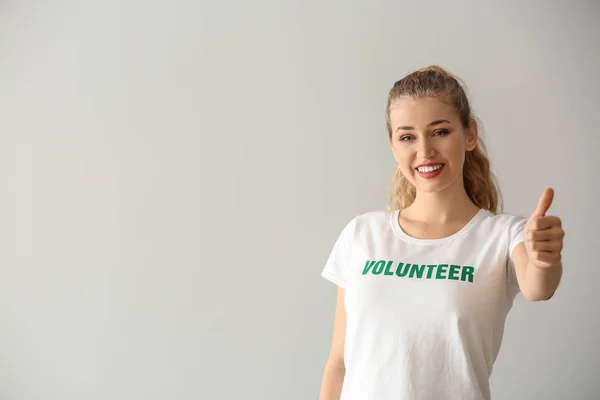 Giovane volontaria che mostra pollice su sfondo chiaro — Foto Stock