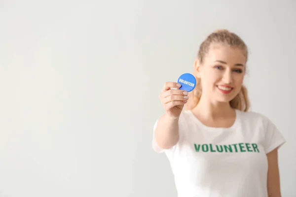 Młoda suczka wolontariuszy z odznaka na jasnym tle — Zdjęcie stockowe